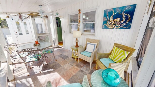 A sunlit room with a dining table, wicker chairs, a lamp, and a painting on the wall. - Under The Tybee Sun | Pet Friendly, Private Pool (Tybee Island)