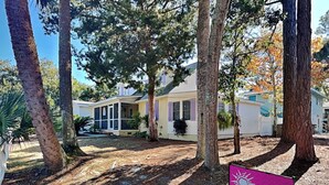 A vacation rental property with a covered porch, a small yard, and a sign advertising vacation rentals. - Under The Tybee Sun | Pet Friendly, Private Pool (Tybee Island)
