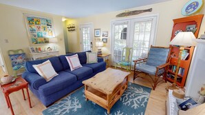 A cozy living room with a blue sofa, wooden coffee table, and a bookshelf. - Under The Tybee Sun | Pet Friendly, Private Pool (Tybee Island)