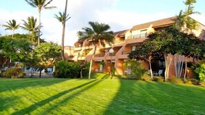 A hotel with a well-maintained lawn, palm trees, and a multi-story building with balconies.