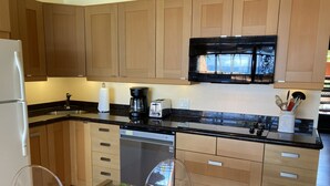 A modern kitchen with wooden cabinets, a black countertop, a coffee maker, a toaster, and a glass-top dining table with a plant.