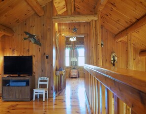 Cozy cabin interior with a television, chair, and wooden bench, set against a high ceiling with exposed beams and a star-shaped decoration.