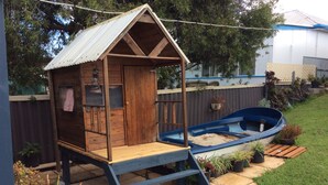 A wooden playhouse with a metal roof, a small boat, and a ladder leading up to the entrance.
