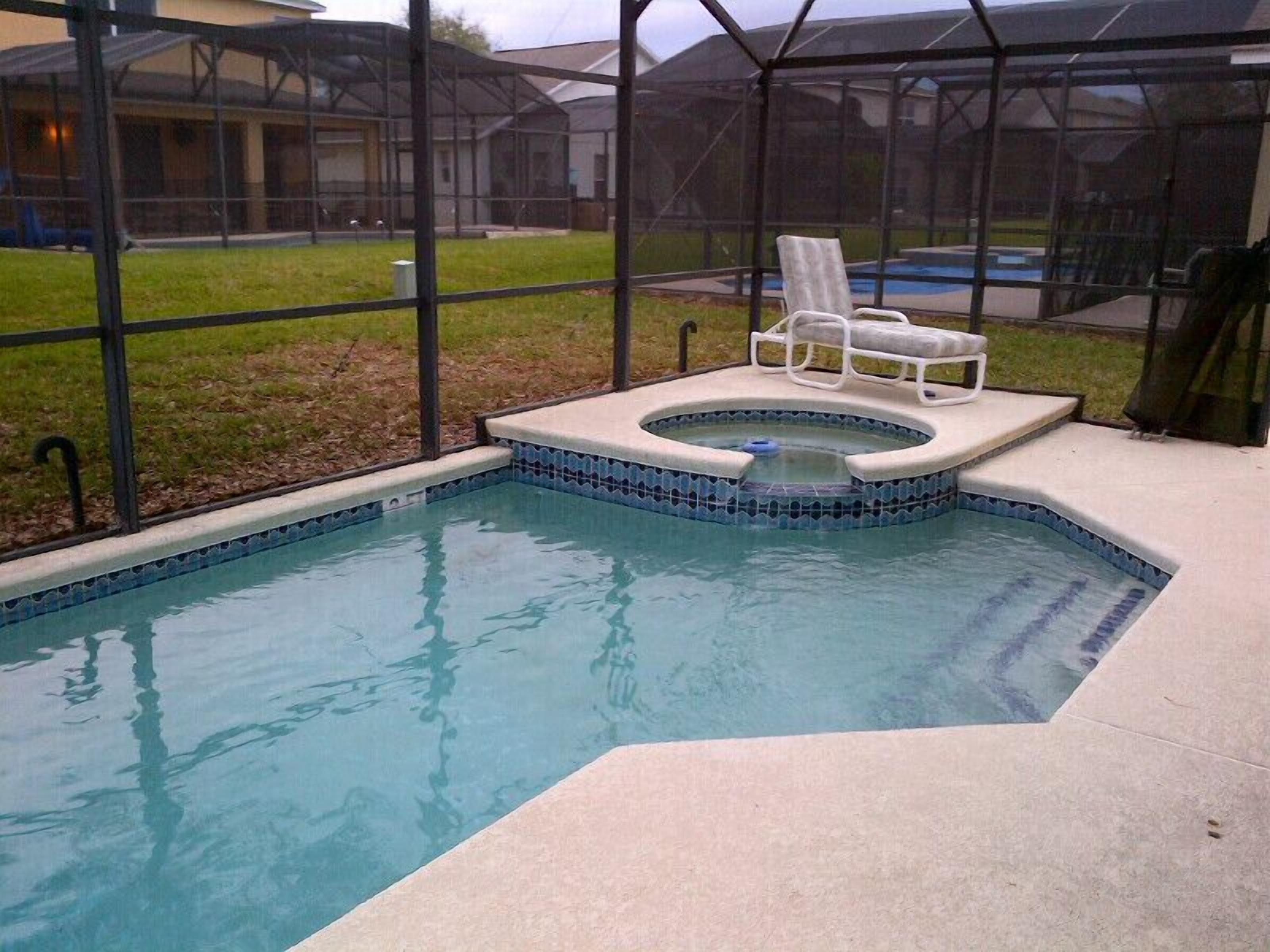 A swimming pool with a hot tub and lounge chairs, surrounded by a glass enclosure.