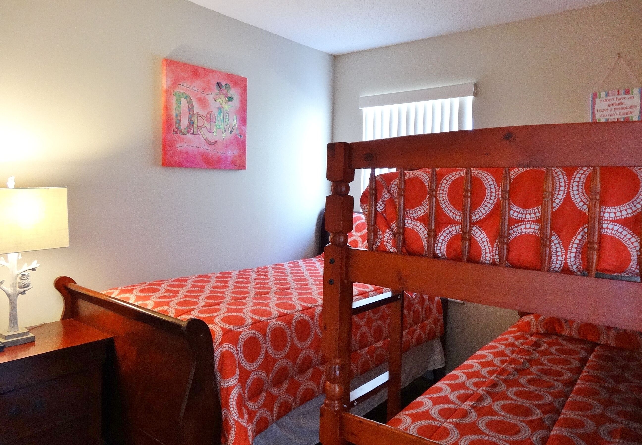 Une chambre avec deux lits simples, une tête de lit en bois, une table de chevet, une lampe et un tableau mural.