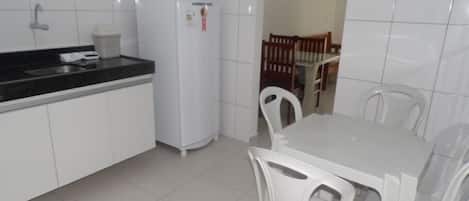 Una pequeña cocina con armarios blancos, un refrigerador blanco, una encimera negra y una mesa de comedor con sillas blancas.