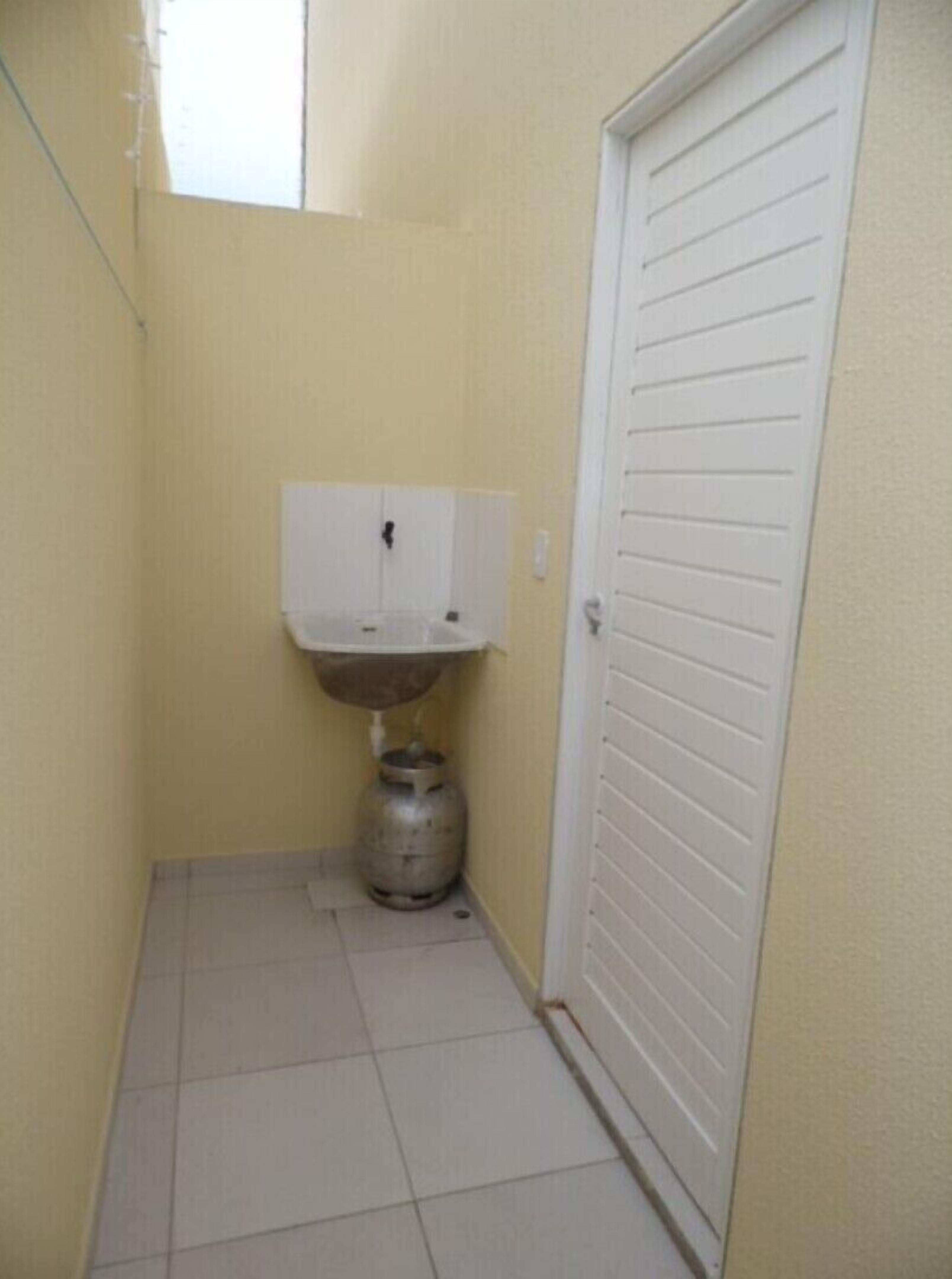 A narrow hallway with a white door, a white sink, and a gas cylinder.