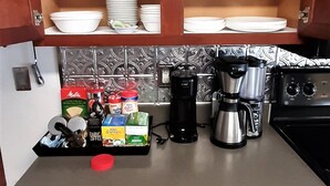Een keuken met houten kastjes, planken met glazen, een koffiezetapparaat en een lade-organizer met keukengerei.
