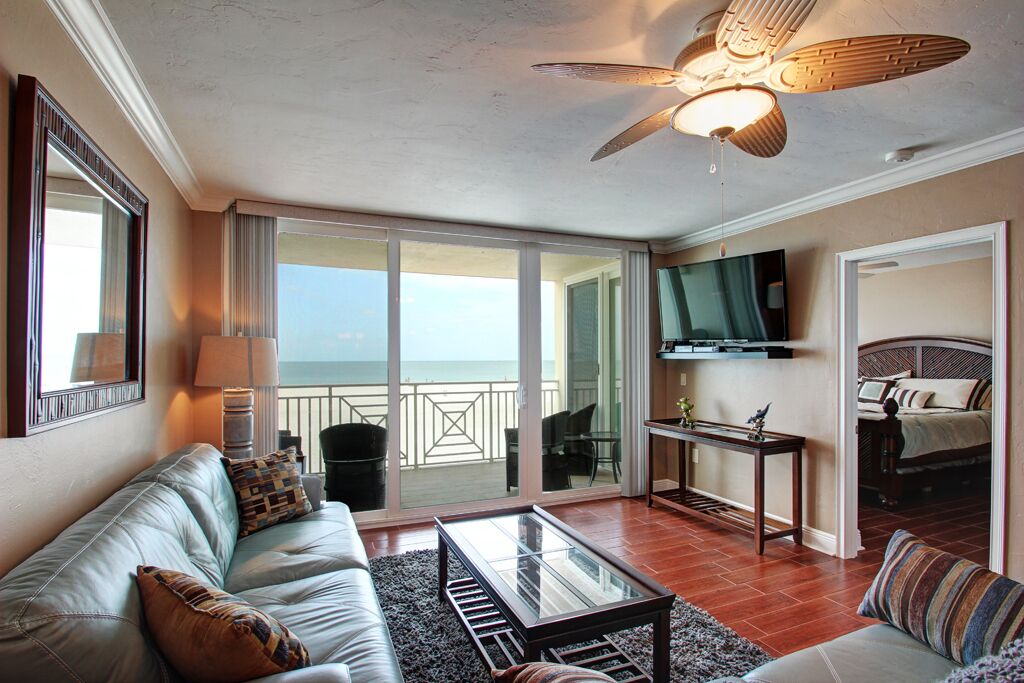 Un salon avec un canapé, une table basse et un ventilateur de plafond. Il y a un balcon avec vue sur l’océan.