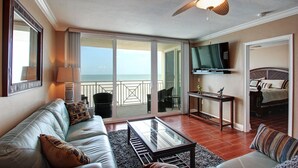 Un salon avec un canapé, une table basse et un ventilateur de plafond. Il y a un balcon avec vue sur l’océan.