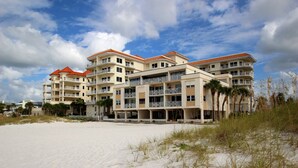 Un hôtel situé en bord de mer, doté de nombreux balcons, avec une plage de sable devant et des palmiers.