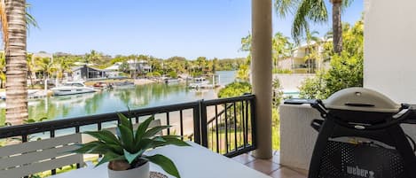 A balcony with a view of a marina, a grill, and a potted plant.