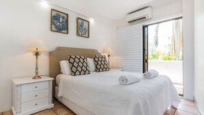 Un letto rifatto con un piumone bianco, due cuscini decorati e due abat-jour. Un comodino bianco con cassetti e una piccola lampada da tavolo. Due opere d'arte incorniciate appendono al muro sopra il letto.