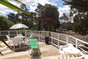 An outdoor patio with white plastic chairs and tables, a striped umbrella, and a red pergola. - Sparkling Cabin Springs (Creswick)