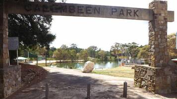 Un arco de piedra con la inscripción "Cattlemen Park" que da acceso a un parque con un estanque y árboles.