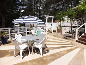 An outdoor patio with a table and chairs, a striped umbrella, and a white fence. - Sparkling Cabin Springs (Creswick)
