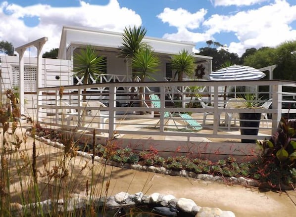 A modern outdoor pool area with lounge chairs, a white fence, and potted plants. - Sparkling Cabin Springs (Creswick)