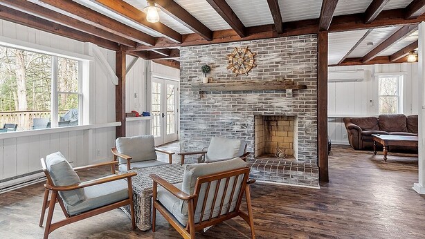 A spacious living room with a stone fireplace, wooden beams, and large windows. - Kennebunkport Summer Rental walk to Dock Square! PET Friendly! (Kennebunkport)