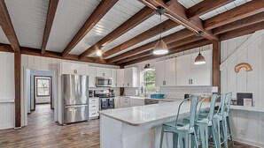 A spacious kitchen with white cabinets, stainless steel appliances, and a central island with bar stools. - Kennebunkport Summer Rental walk to Dock Square! PET Friendly! (Kennebunkport)