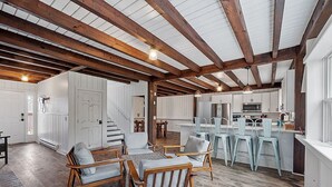 A spacious kitchen with wooden beams, a dining area with light-colored chairs, and a view of the kitchen through an open door. - Kennebunkport Summer Rental walk to Dock Square! PET Friendly! (Kennebunkport)