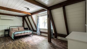 A bedroom with a sloped ceiling, wooden beams, a bed with a metal frame, a nightstand, and a window with curtains.