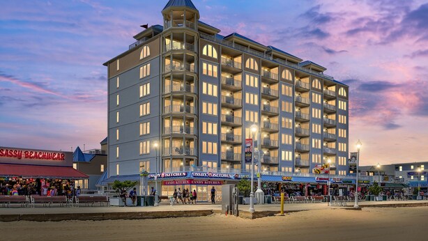 Ett hotell med flera våningar, balkonger, ett centralt torn och en strandpromenad med butiker.