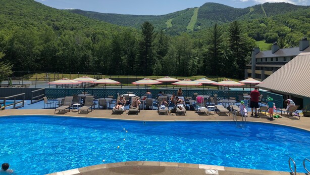 A swimming pool with lounge chairs and umbrellas, surrounded by a mountainous landscape.