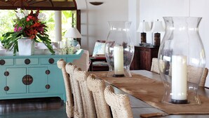 A dining area with a teal-colored cabinet, clear glass vases with candles, and a woven chair. - Elegant Villa in Private Hope Bay. Infinity Pool with Sea View. (Bequia)