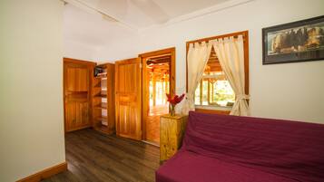 Um quarto com piso de madeira, uma cama com cobertura vermelha, um guarda-roupa de madeira, um armário de madeira e uma escada de madeira que leva a um espaço aberto.