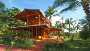 Una casa de madera con balcón, rodeada de exuberante follaje y palmeras.