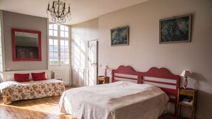 Un dormitorio con una cama grande, dos camas más pequeñas, un candelabro y obras de arte en las paredes.
