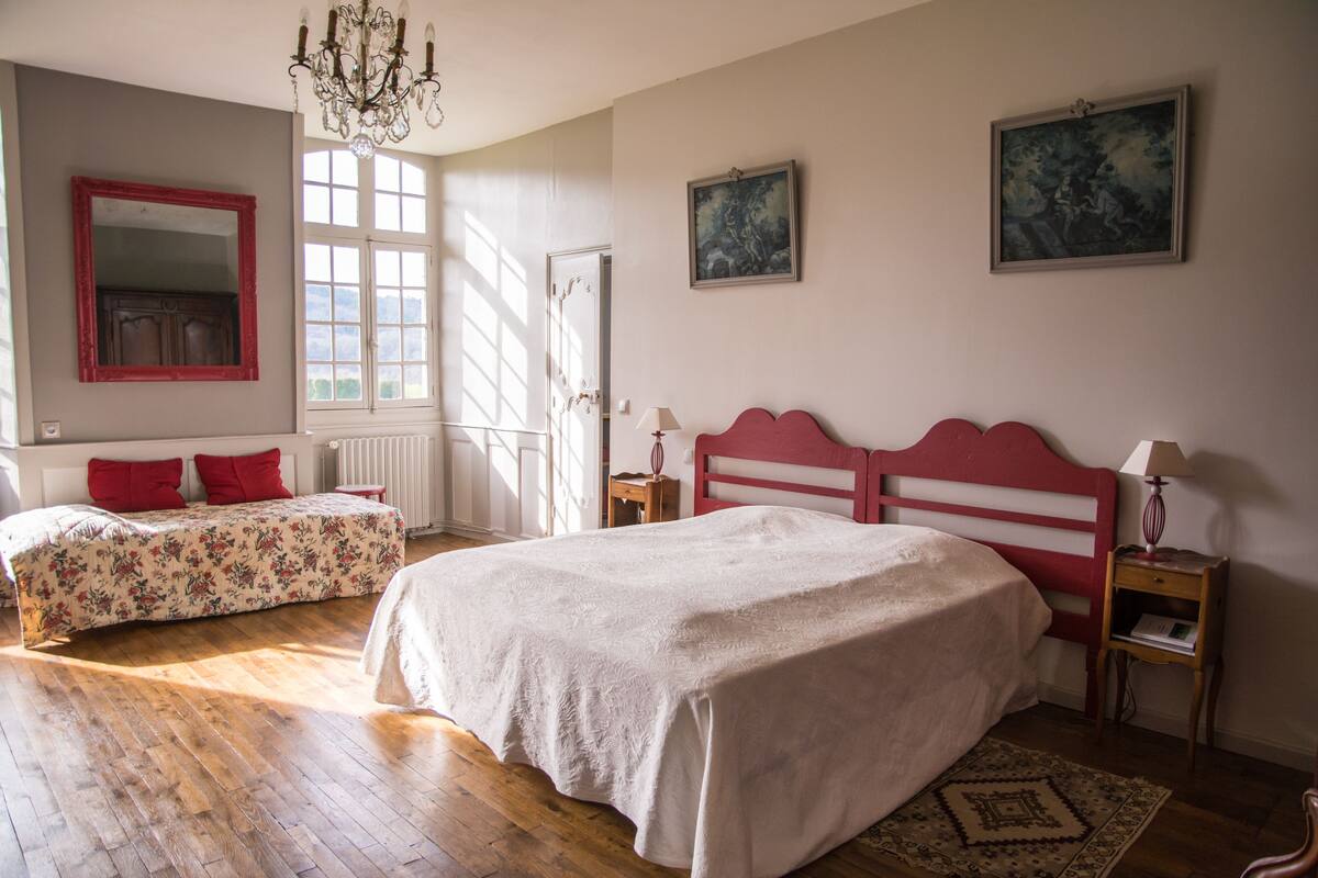 Ein Schlafzimmer mit einem großen Bett, zwei kleineren Betten, einer Chandelierleuchtre und Kunstwerken an den Wänden.