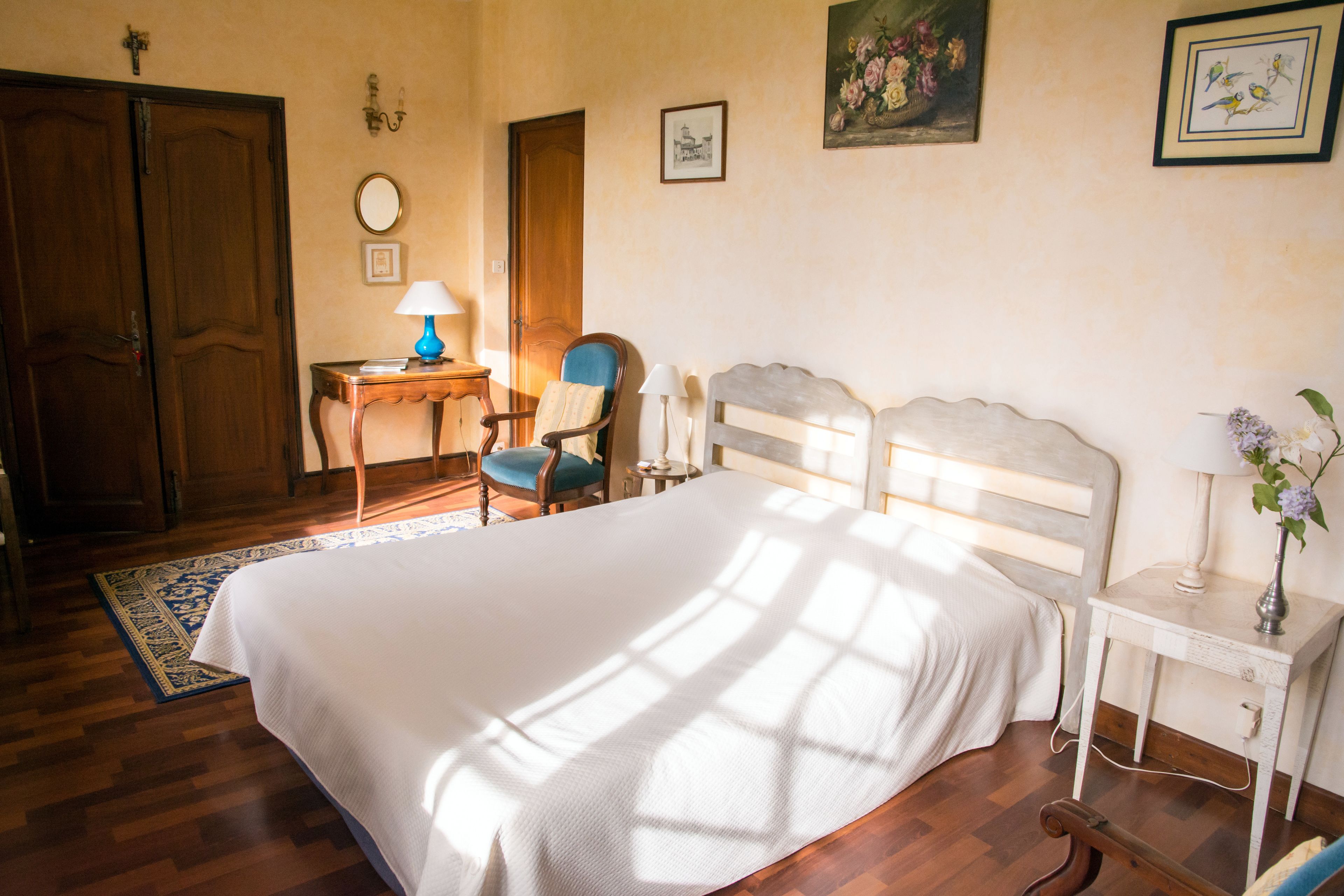 Een slaapkamer met een groot bed, een houten garderobe, een bureau met een lamp en een stoel.