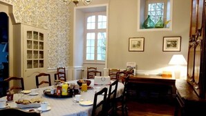 Comedor con una mesa dispuesta para el desayuno, sillas de madera, una araña y una ventana con vistas.