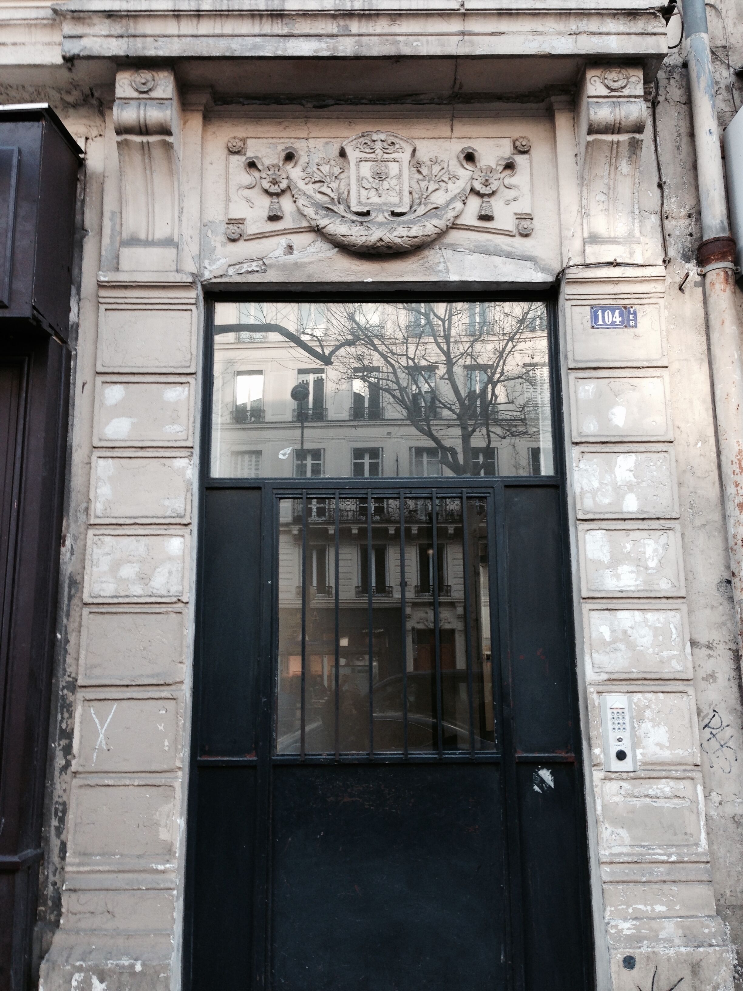 A building facade with a black gate, a plaque with the number 104, and a window reflecting another building.