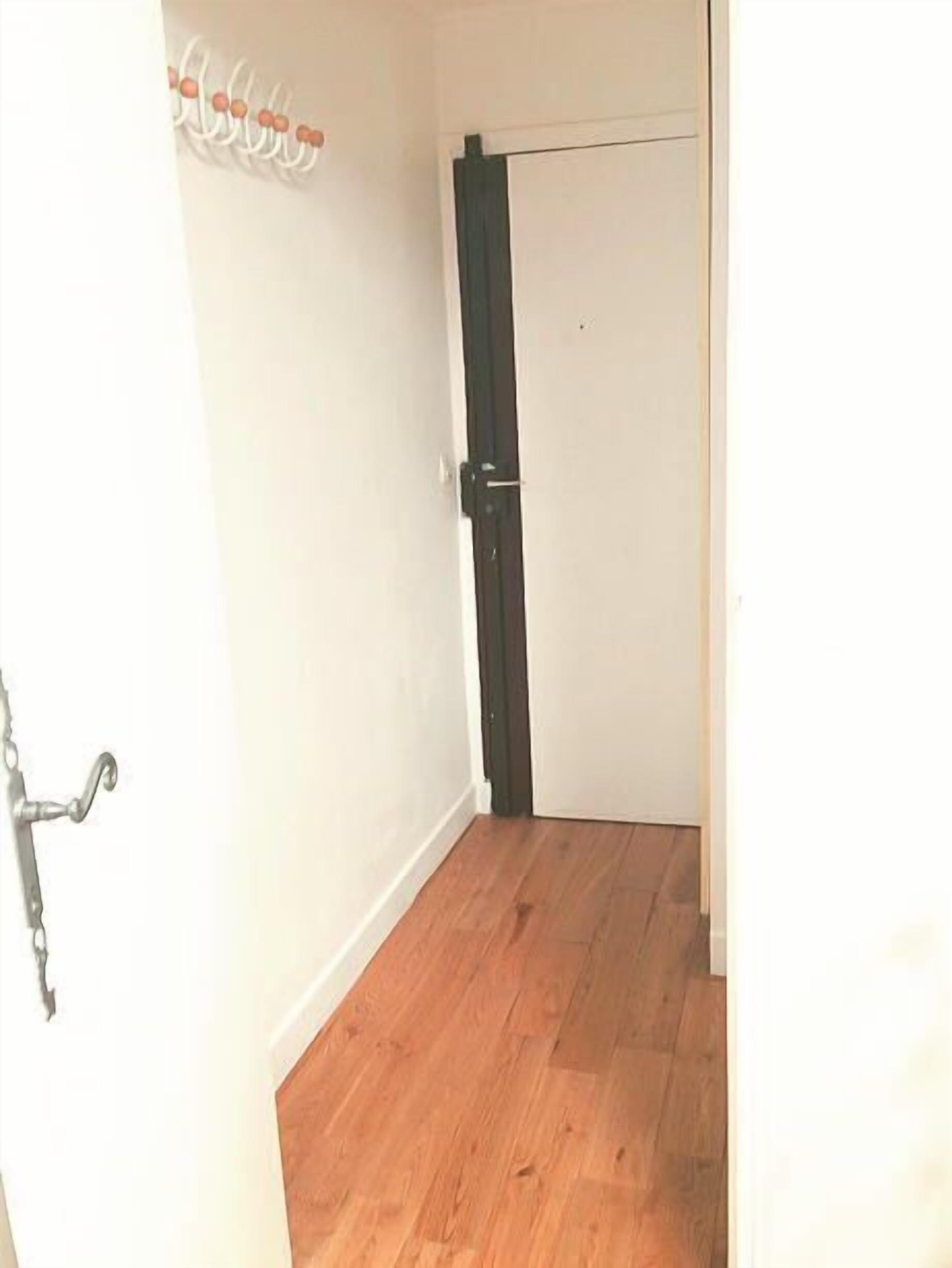 Un couloir étroit avec un plancher en bois, une porte blanche et une porte noire.