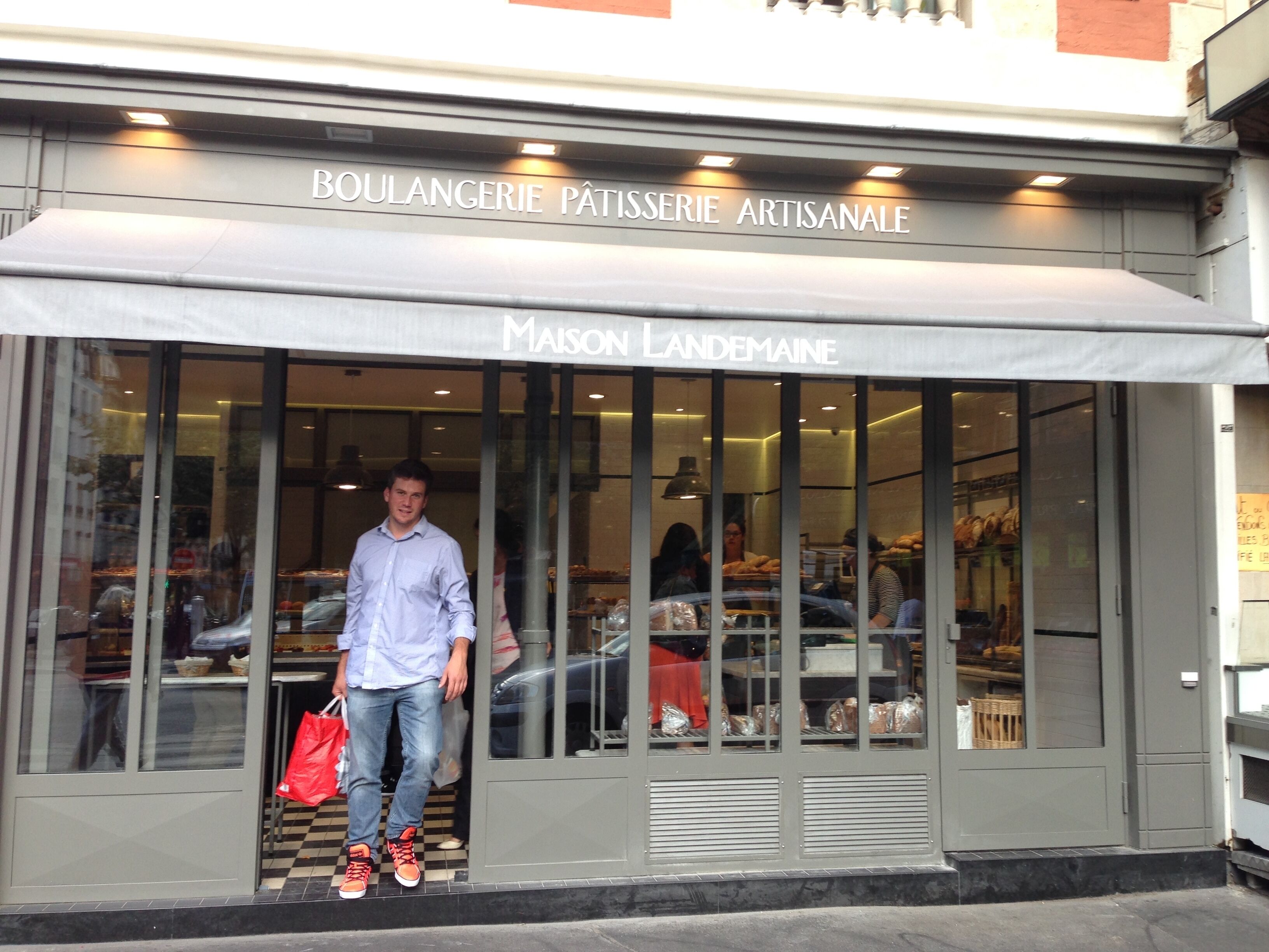 Un escaparate con un letrero que dice 'BOULANGERIE PÂTISSERIE ARTISANALE' y 'Maison Landemaine' visible a través del cristal.