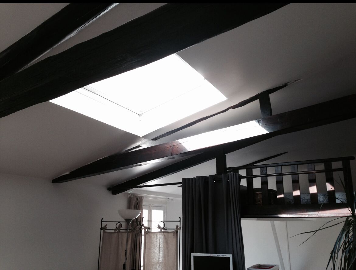 A room with exposed wooden beams, a skylight, a bed with a headboard, and a window with curtains.