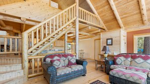 Un interior de madera con una escalera, dos sofás con cojines estampados y una lámpara.