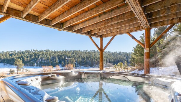 Un jacuzzi bajo una pérgola de madera con un paisaje nevado al fondo.