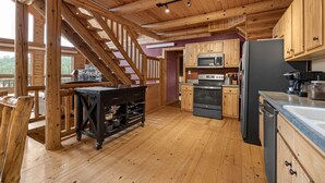 Cocina de cabaña de madera con chimenea de piedra, armarios de madera y refrigerador negro.