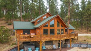 Una cabaña de troncos con terraza, mobiliario exterior y cimientos de piedra.