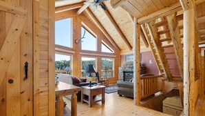 Interior de una cabaña de madera con habitación en altillo, chimenea y comedor.
