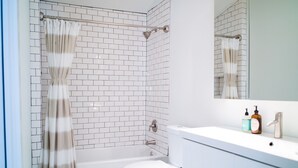 Un bagno moderno con piastrelle bianche a metro, una doccia con porta in vetro, un WC bianco e un mobile lavabo con specchio e articoli da toilette.