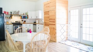 Una cucina moderna con mobili bianchi, una parete d'accento in legno e un'area pranzo con tavolo e sedie in legno chiaro.