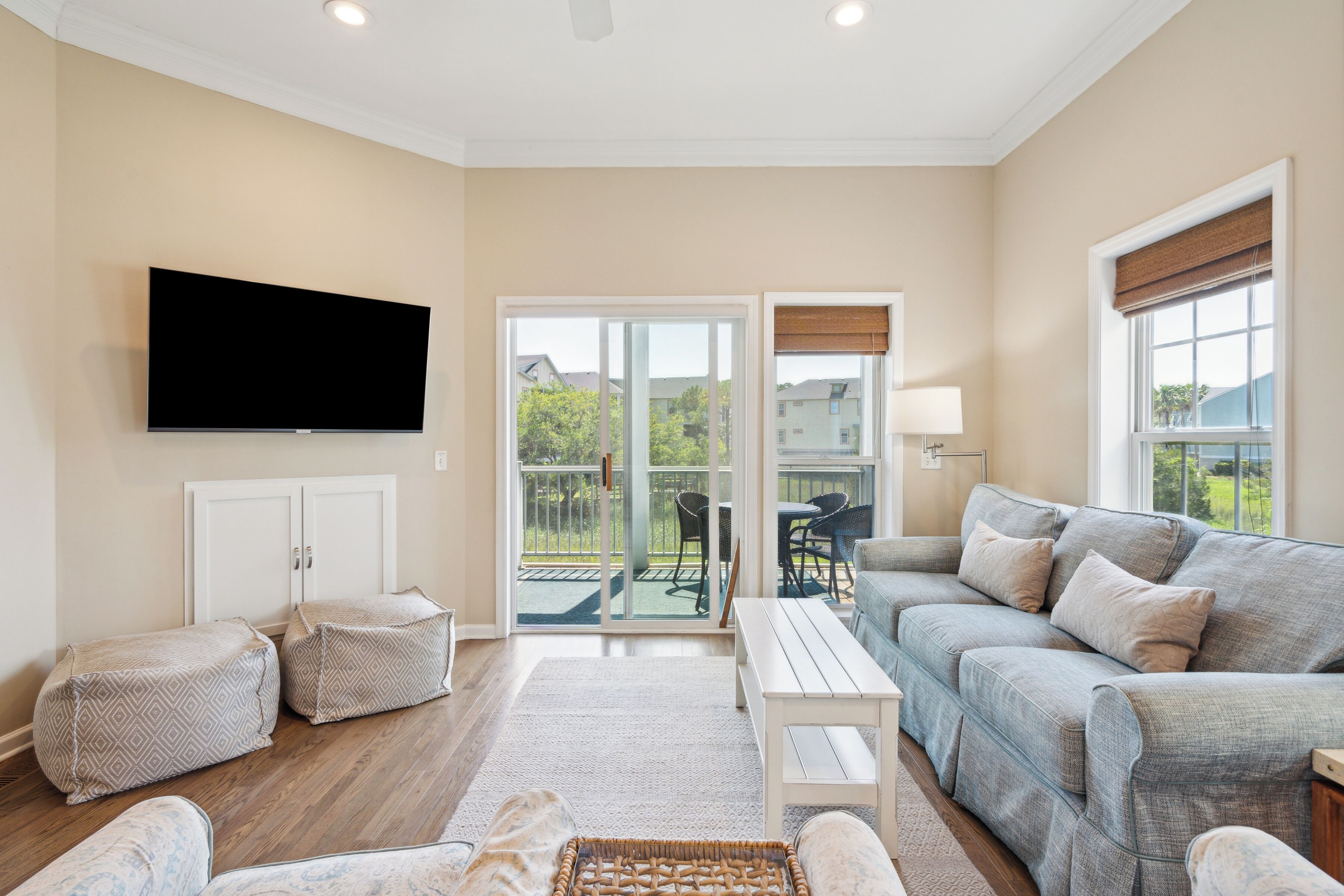 A living room with a flat-screen TV, a grey sofa, a coffee table, and a patterned ottoman.