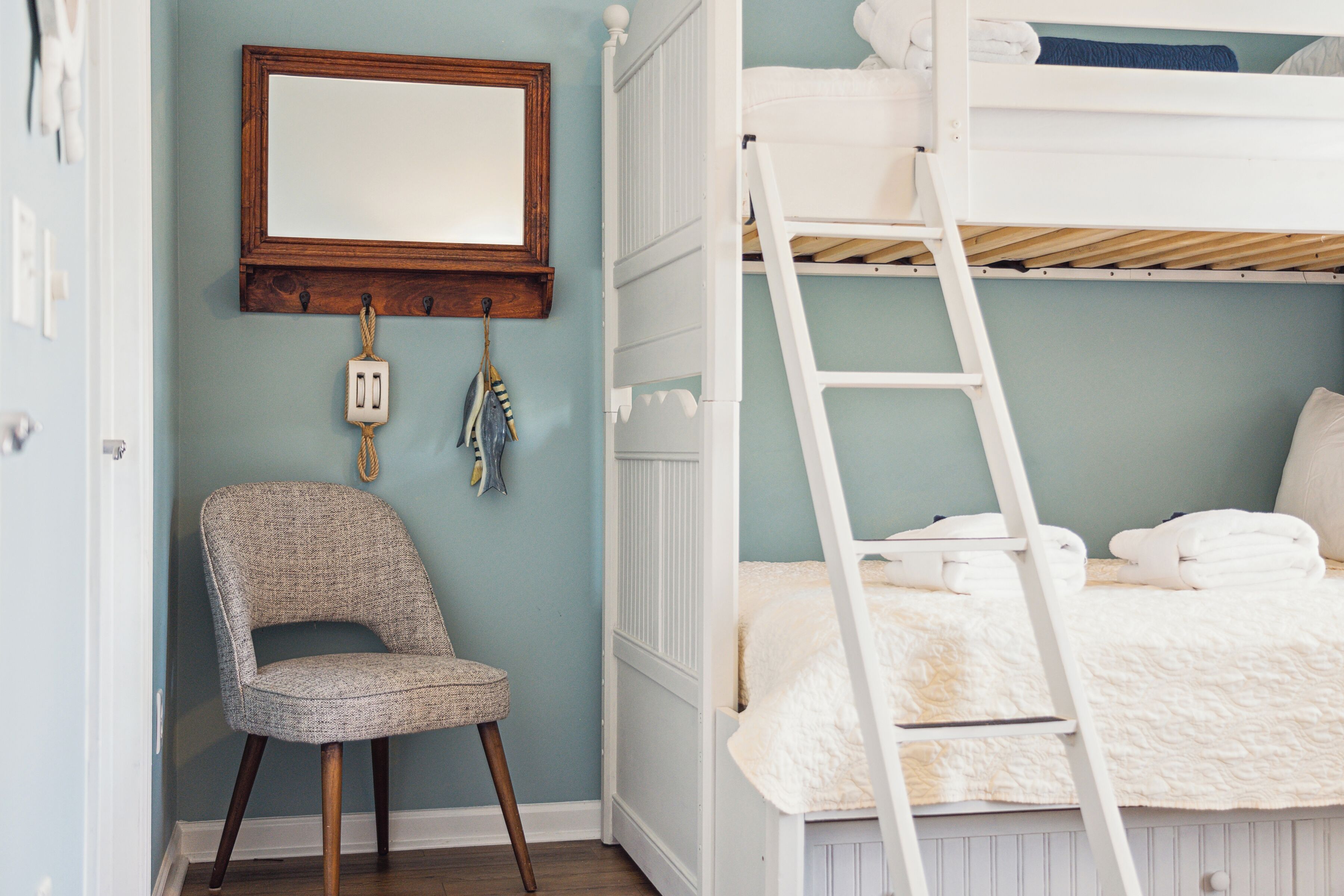 Un dormitorio con una cama litera, una silla, una escalera y un espejo en la pared.