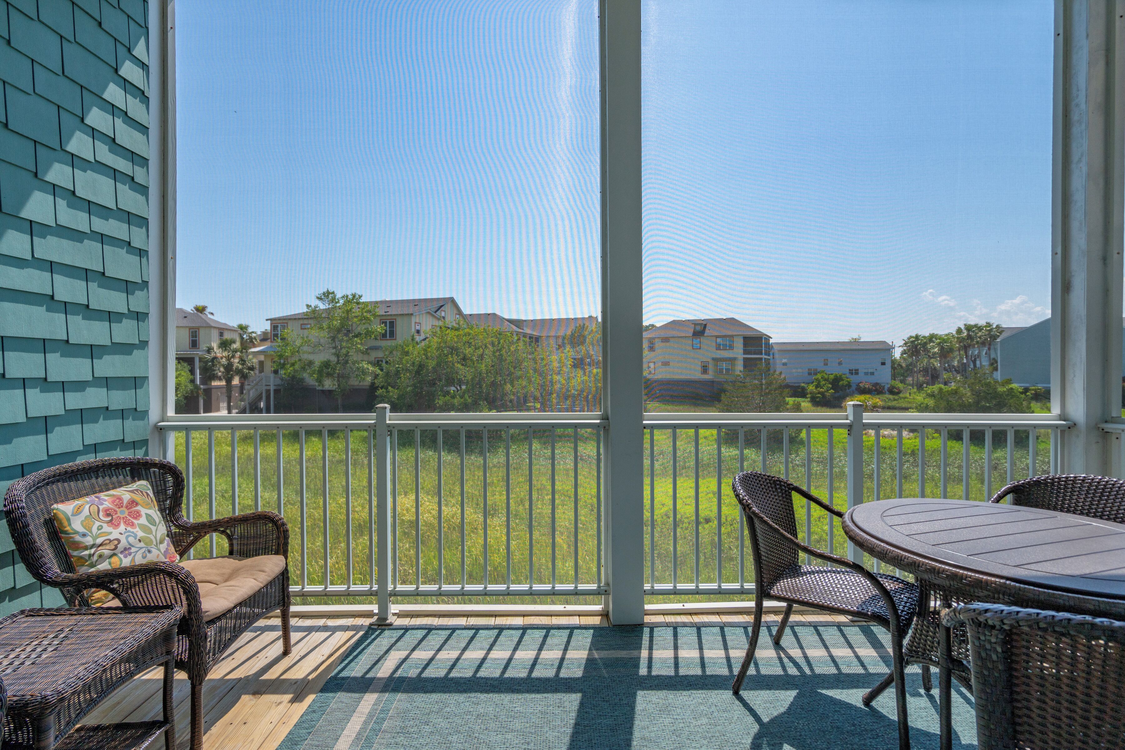 A covered outdoor area with wicker furniture, a table, and a view of a residential neighborhood.