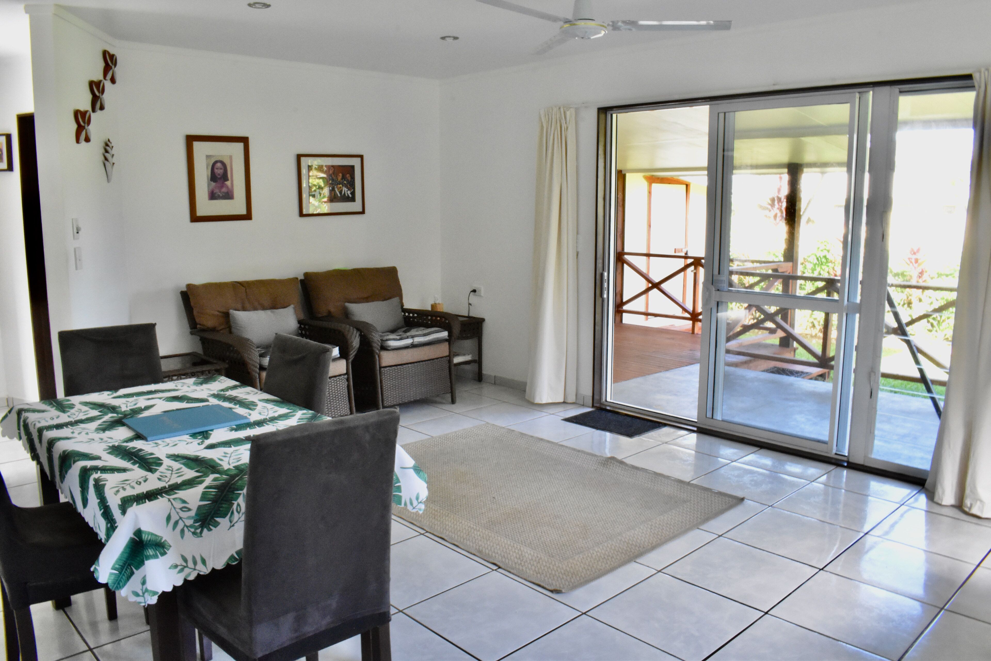 A room with a bed, a dining table with chairs, a small table with a chair, a rug, and a sliding glass door leading to an outdoor area.