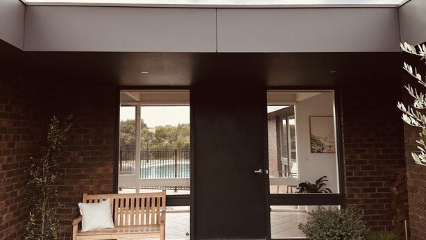 A modern house with a dark entrance, a wooden bench, and potted plants. - Devonlea Olive Grove
4br Home with pool on 8acres- next door to The Cups Estate (Fingal)